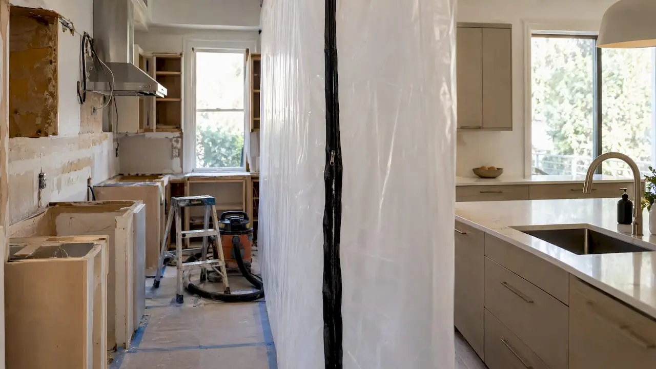 Floor-to-ceiling plastic containment wall with a zipper door sealing off a kitchen remodel